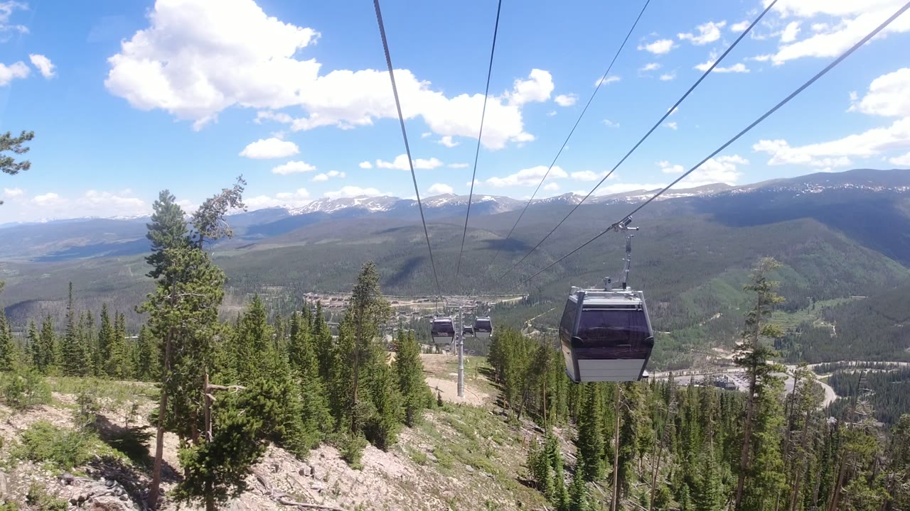 Several gondola cabins recede along cables over forest and rocky ground in Winter Park, Colorado, with broad mountain ridges in the background and no visible people.