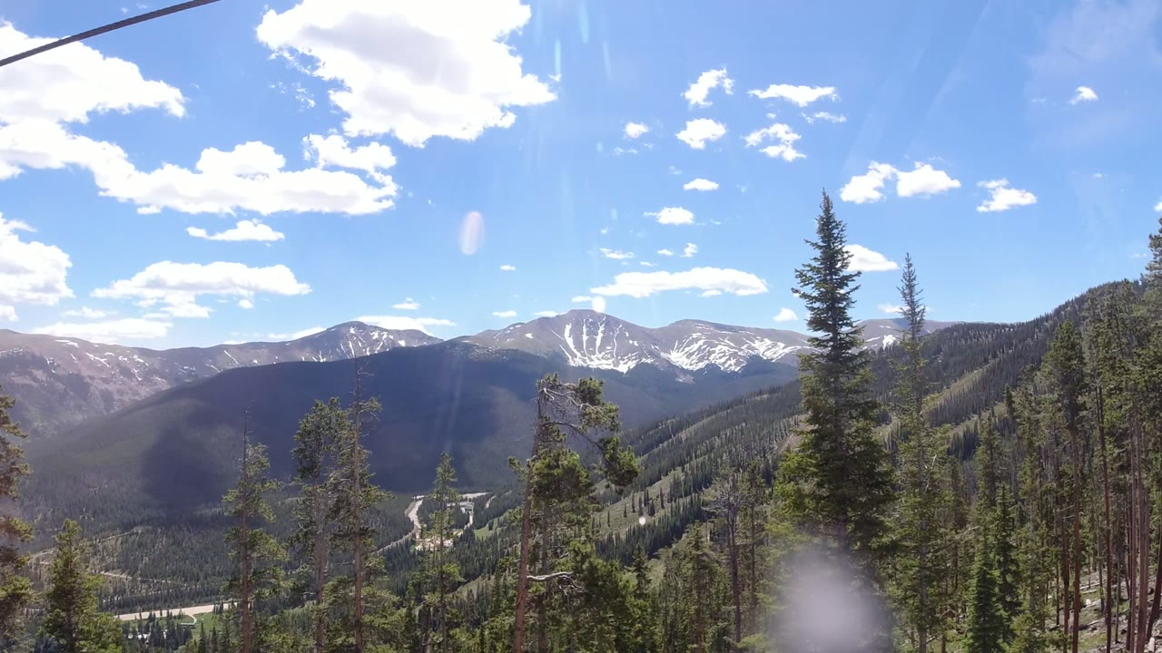 Wide mountain valley with pine trees, cable line, blue sky, and clouds