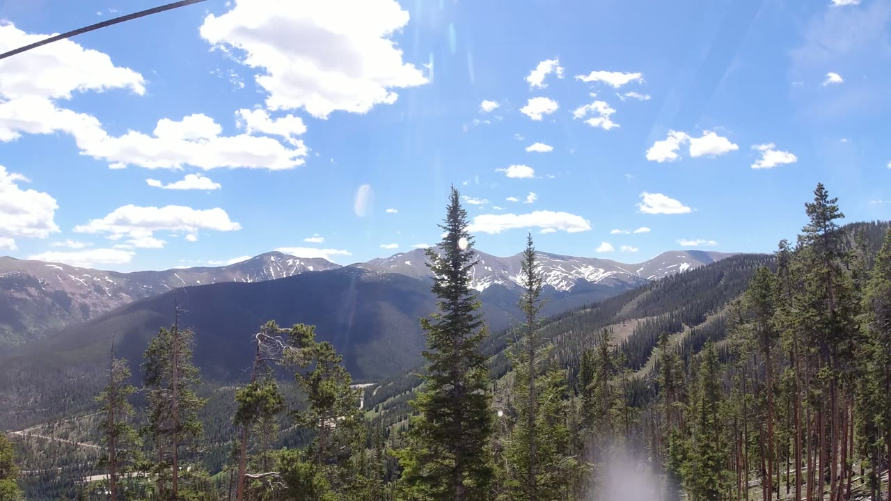 Winter Park, Colorado ridgelines and evergreen slopes fill the frame beneath a dark overhead cable, with bright clouds and no visible people.