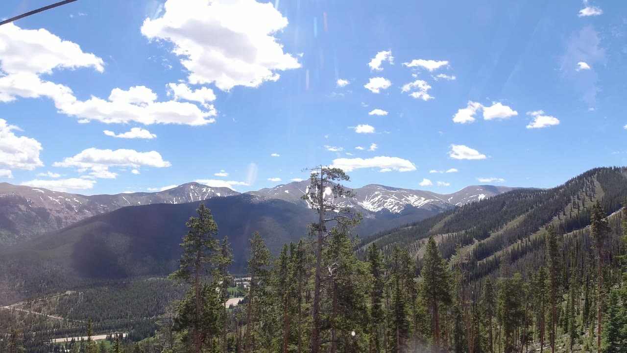 Evergreen forest and snow-dusted mountains under a blue sky.