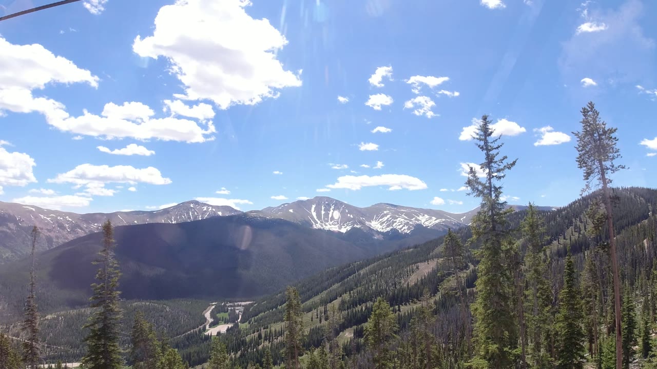 Second view of the Winter Park, Colorado valley with a broad ridgeline, snow markings on distant peaks, foreground pine trunks, and no visible people.
