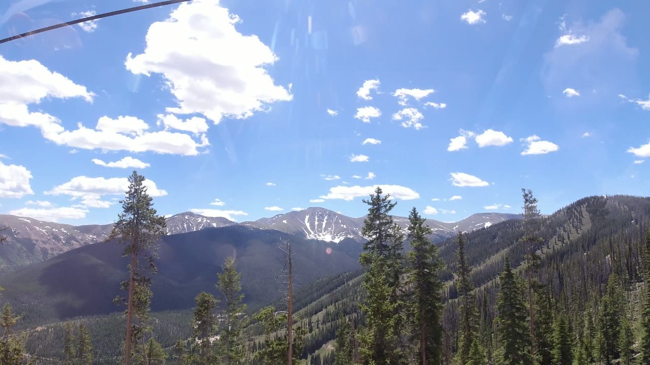 Early frame looking across Winter Park, Colorado forested slopes toward distant ridges, with the lift cable crossing near the top and no visible people.
