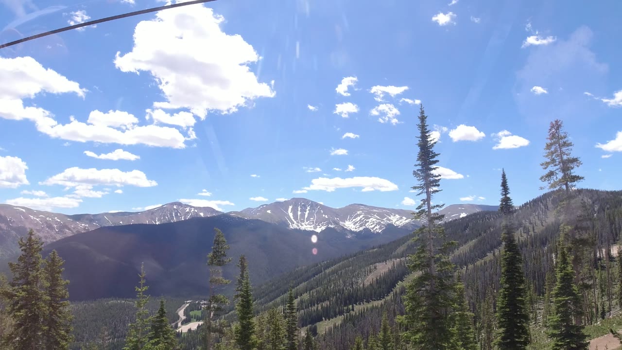 Wide view of snow-streaked mountains and evergreen slopes in Winter Park, Colorado, with blue sky, window reflections, and no visible people.