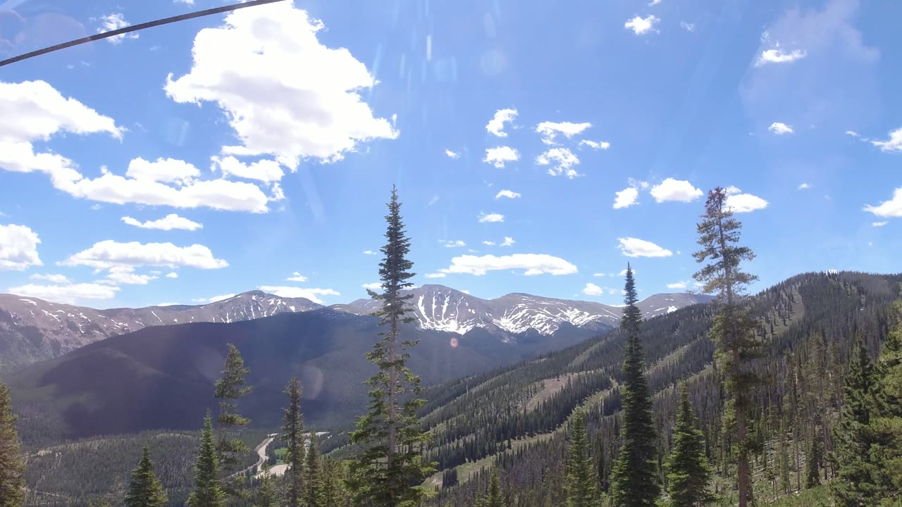 Winter Park, Colorado mountain view with tall evergreens in the foreground, layered ridges in the distance, bright clouds, and no visible people.