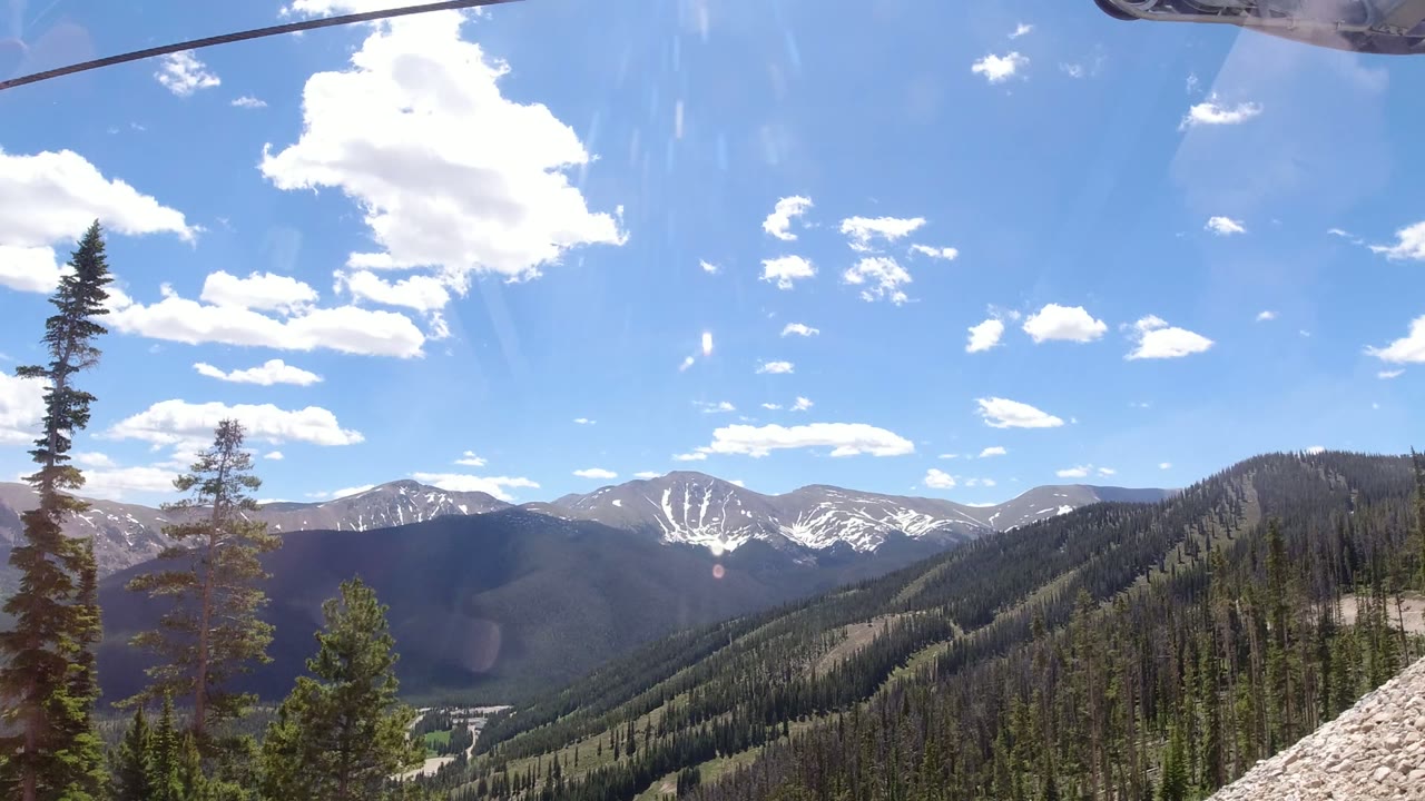 Mountain ridges and evergreen slopes under a blue sky with ski lift cable overhead.