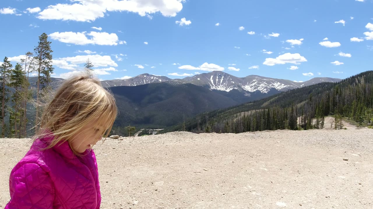 Young girl in a magenta jacket on a rocky mountain overlook.