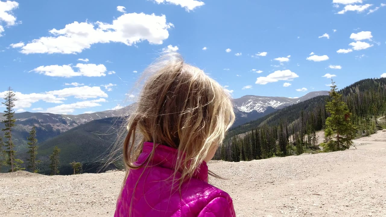 Child in a pink jacket near a mountain path under a blue sky.