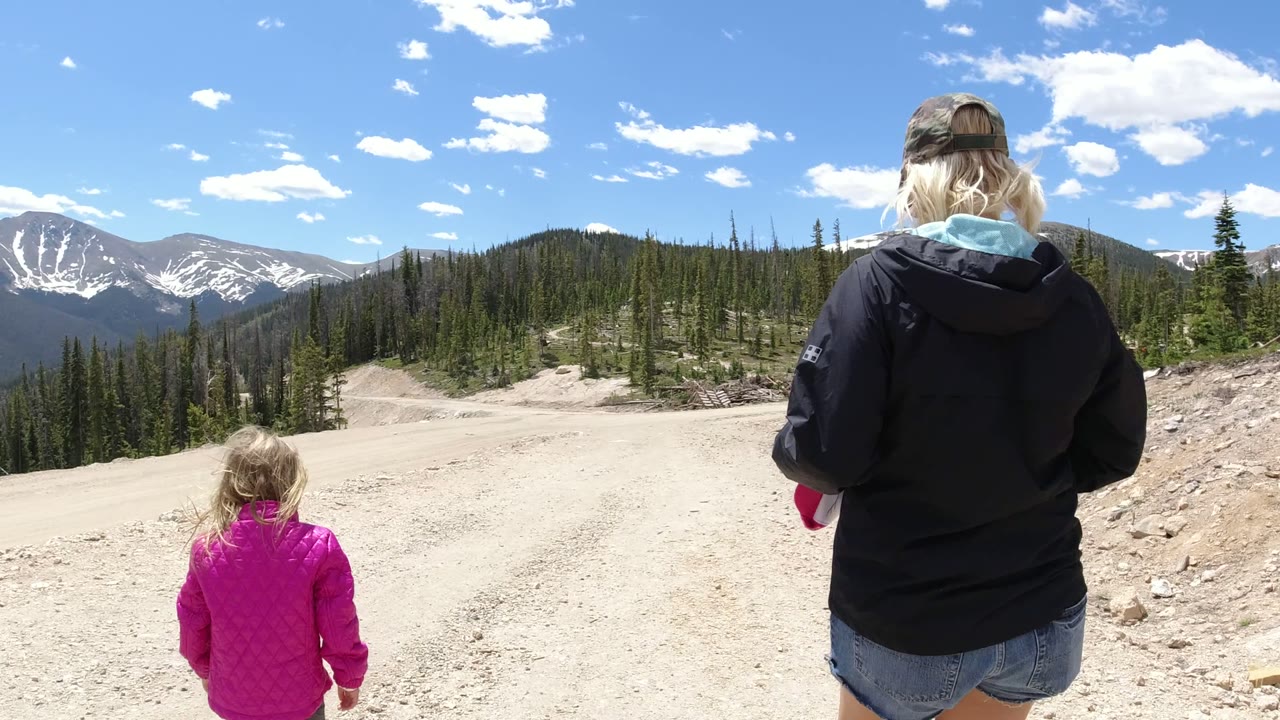 Adult and child walking on a gravel mountain road with peaks ahead.