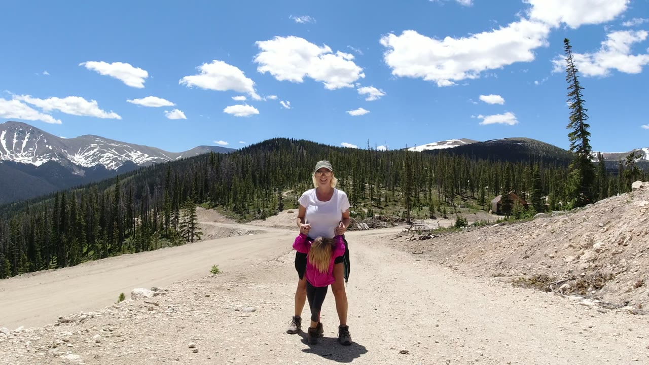 Woman holding a young girl on a sunny dirt mountain road.