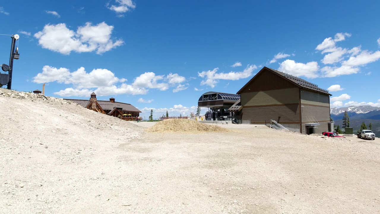 Gravel slope with mountain buildings and ski-lift structure under blue sky.
