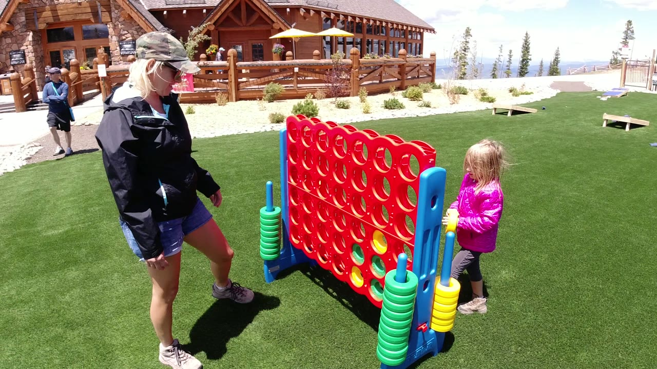 At Winter Park, Colorado, the woman stands to the left of the red game board while the young girl remains at the right side near the blue frame and stacked yellow pieces.
