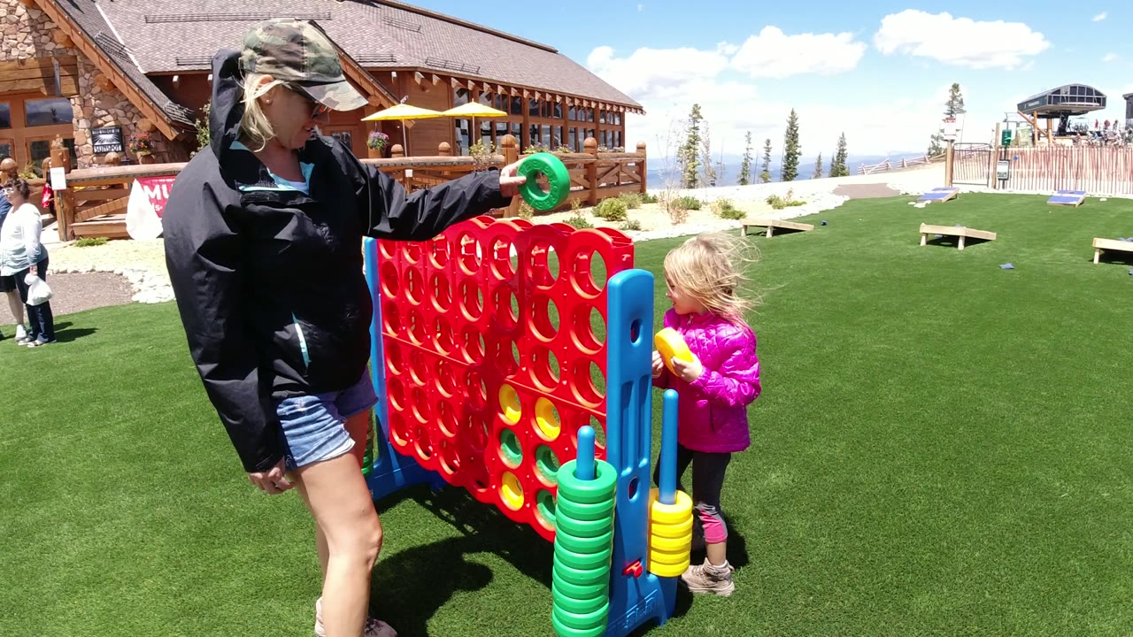 In Winter Park, Colorado, the woman raises a green game disc over the red Connect Four grid while the young girl in pink stands beside the board.