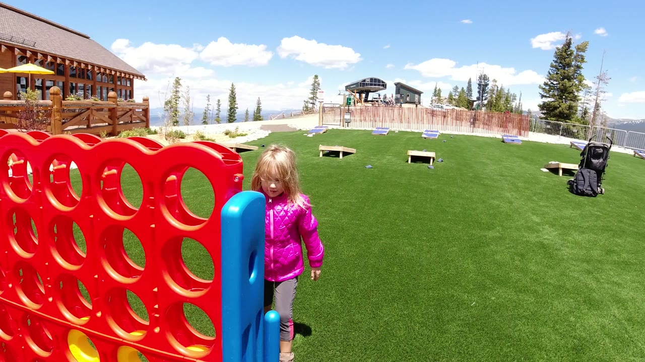 Young girl in a pink jacket beside a giant red lawn game on grass.