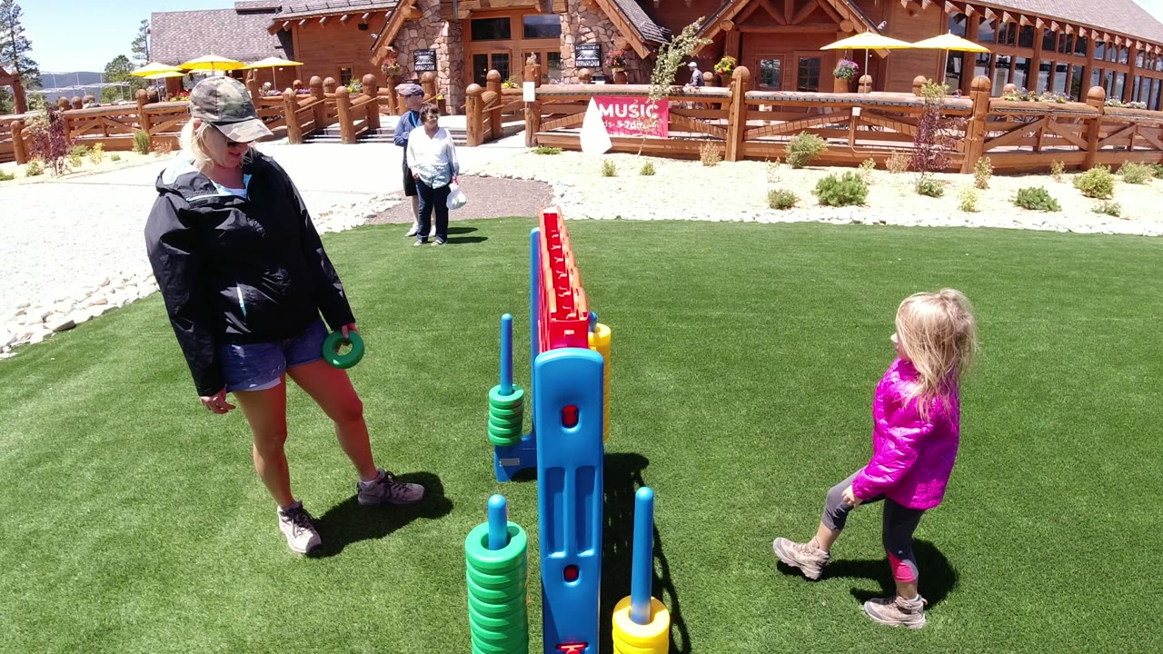 Young girl and adult standing by a large outdoor game on artificial turf.