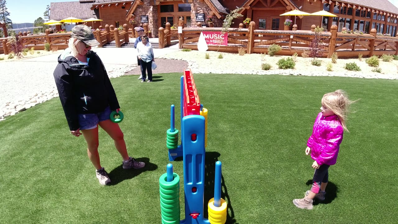 The adult stands with a green disc near the oversized game while the young girl watches from several feet away in Winter Park, Colorado.