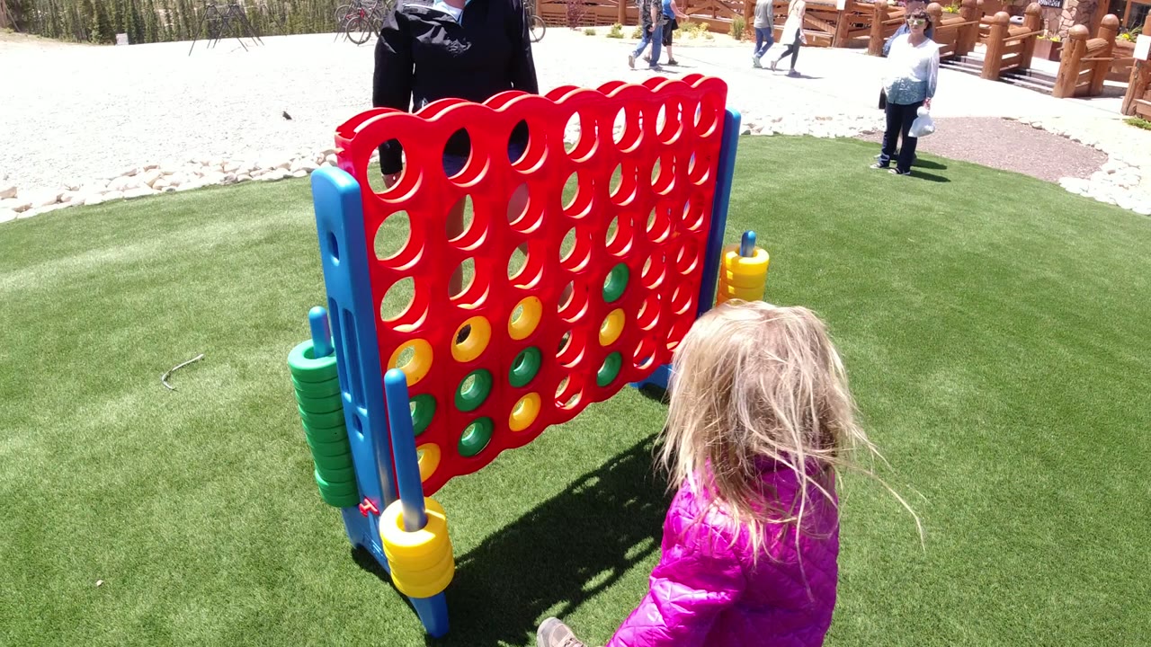 Young girl near a large red Connect Four game on green turf.