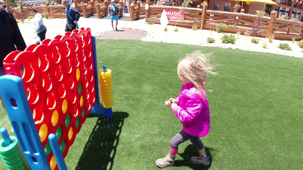 Girl in a pink jacket near a giant red game board on green turf.