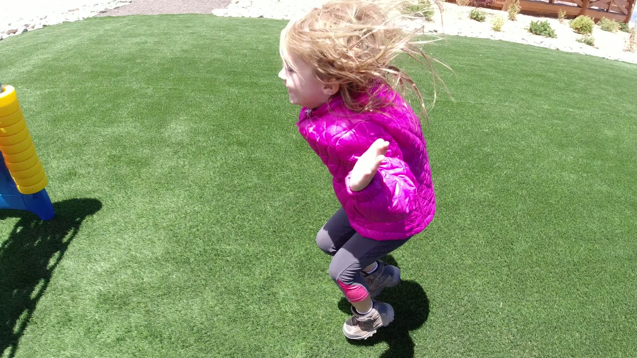 Young girl in pink jacket running on green park grass.
