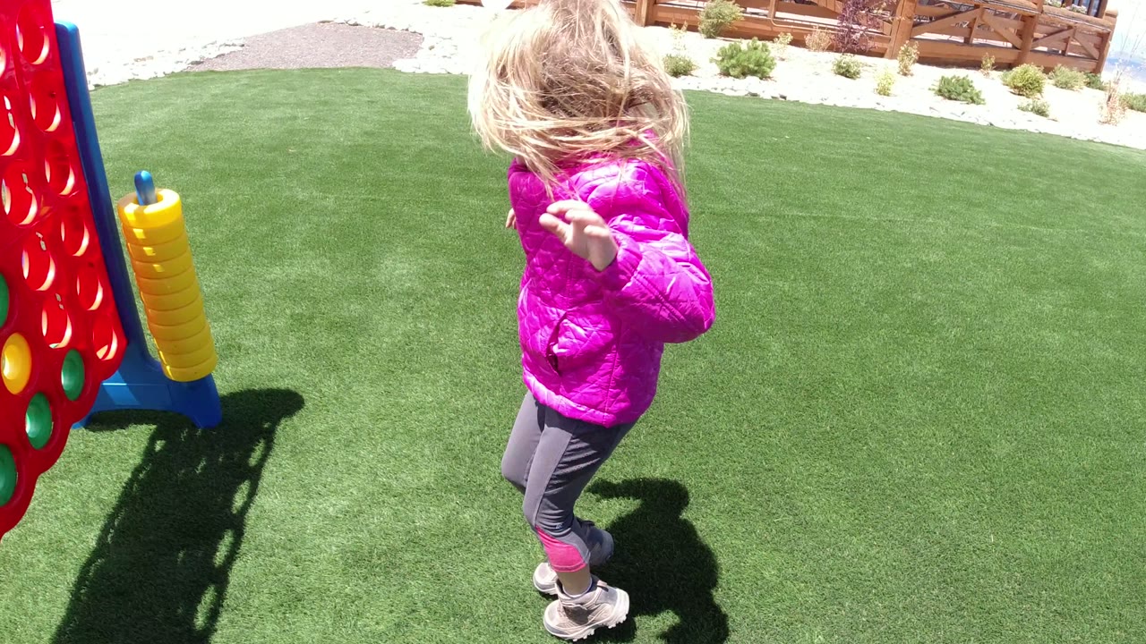 The girl passes near a red Connect Four-style game with yellow side pieces on the green lawn in Winter Park, Colorado.