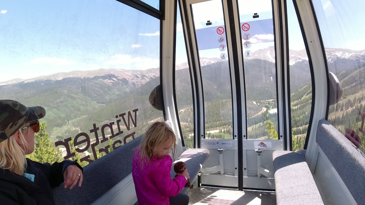 Woman and young girl inside a gondola with mountain views through the windows.