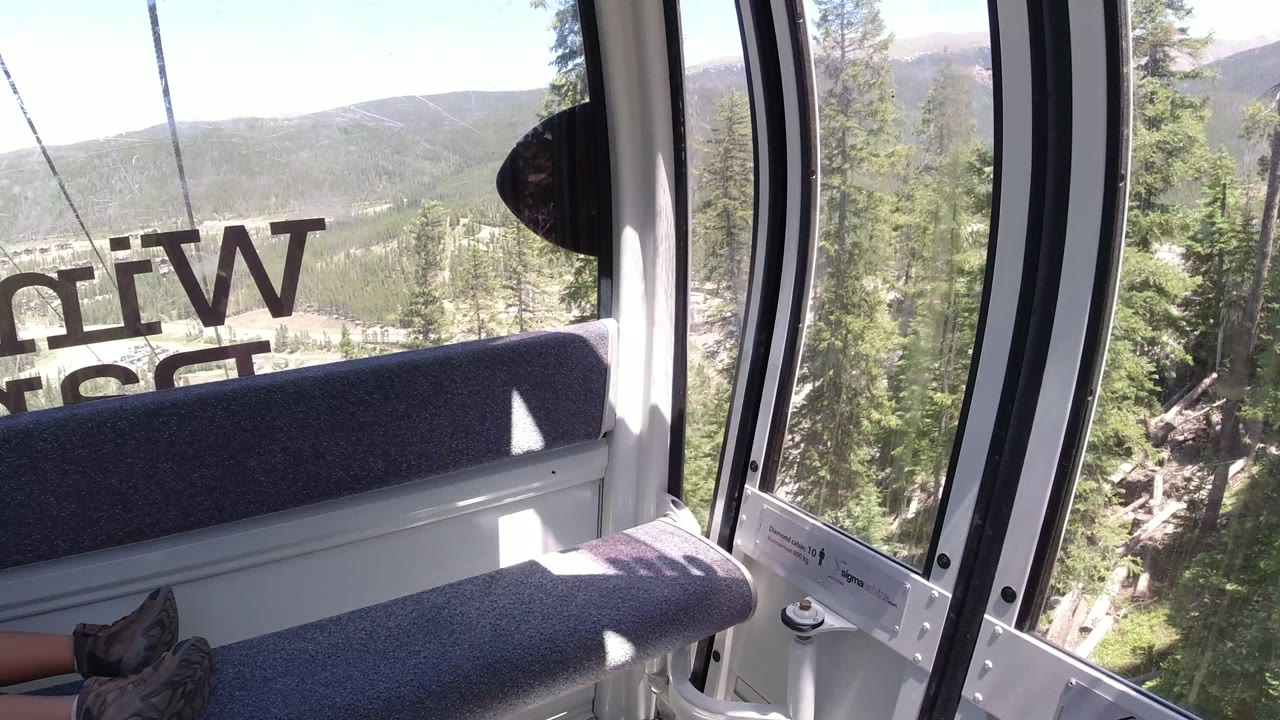 Cable car interior with bench, window lettering, trees, and distant mountains.