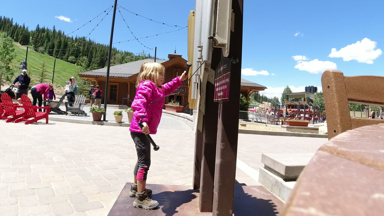 Child in a pink jacket holding a toy beside a patio post.