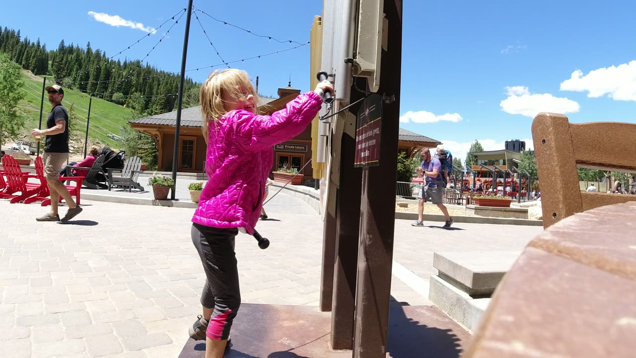 Child in a pink jacket reaches toward an outdoor activity board.