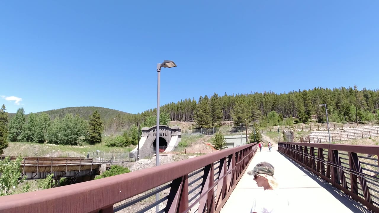Forward view from the bridge in Winter Park, Colorado, with the tunnel entrance slightly left of center, a tall lamp post above the walkway, and a partial person near the lower edge.