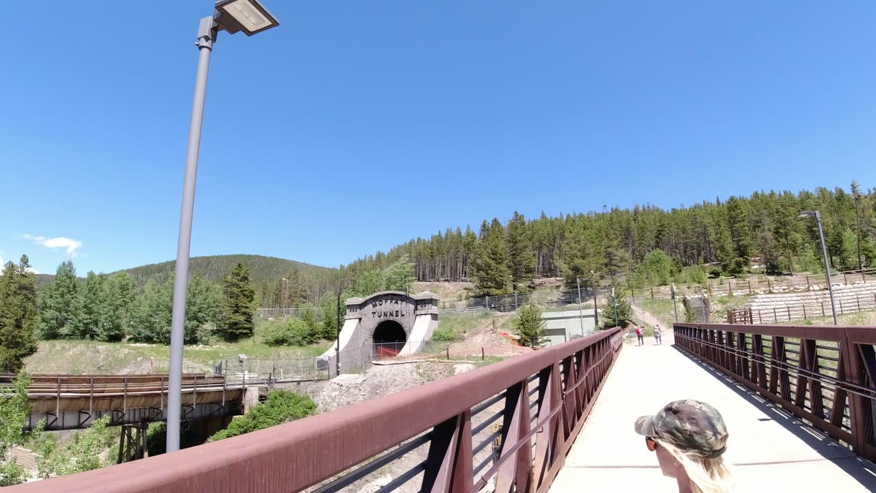Pedestrian bridge railing leading toward a tunnel entrance and forested hillside.