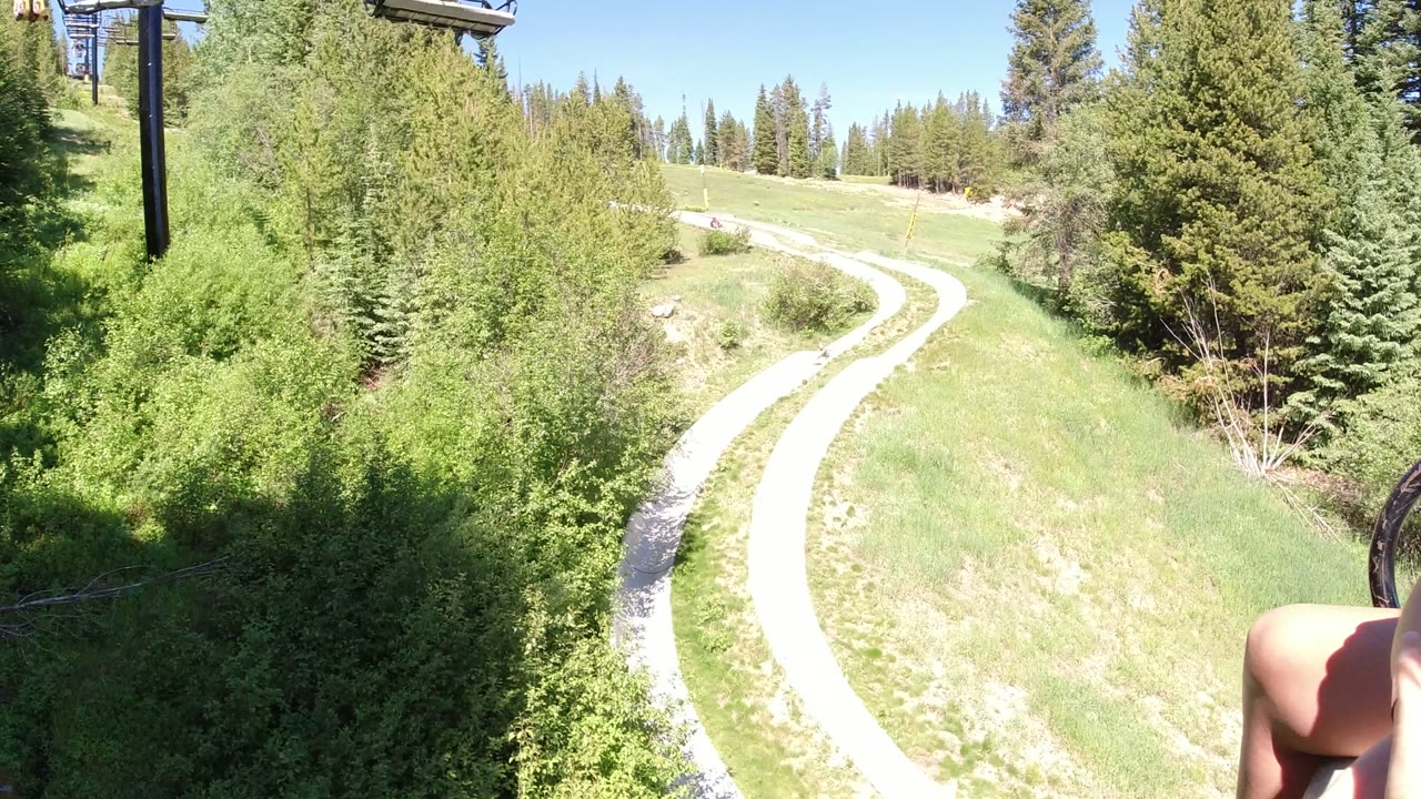 A bright winding path runs through trees in Winter Park, Colorado, with lift structure partly visible at the top and no clear faces in view.