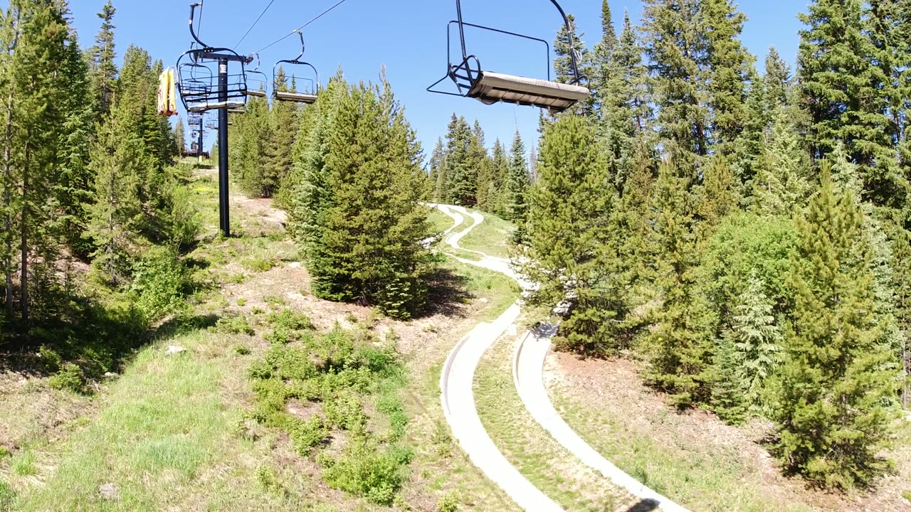 Chairlift seats above a forested hillside and curving pale path.