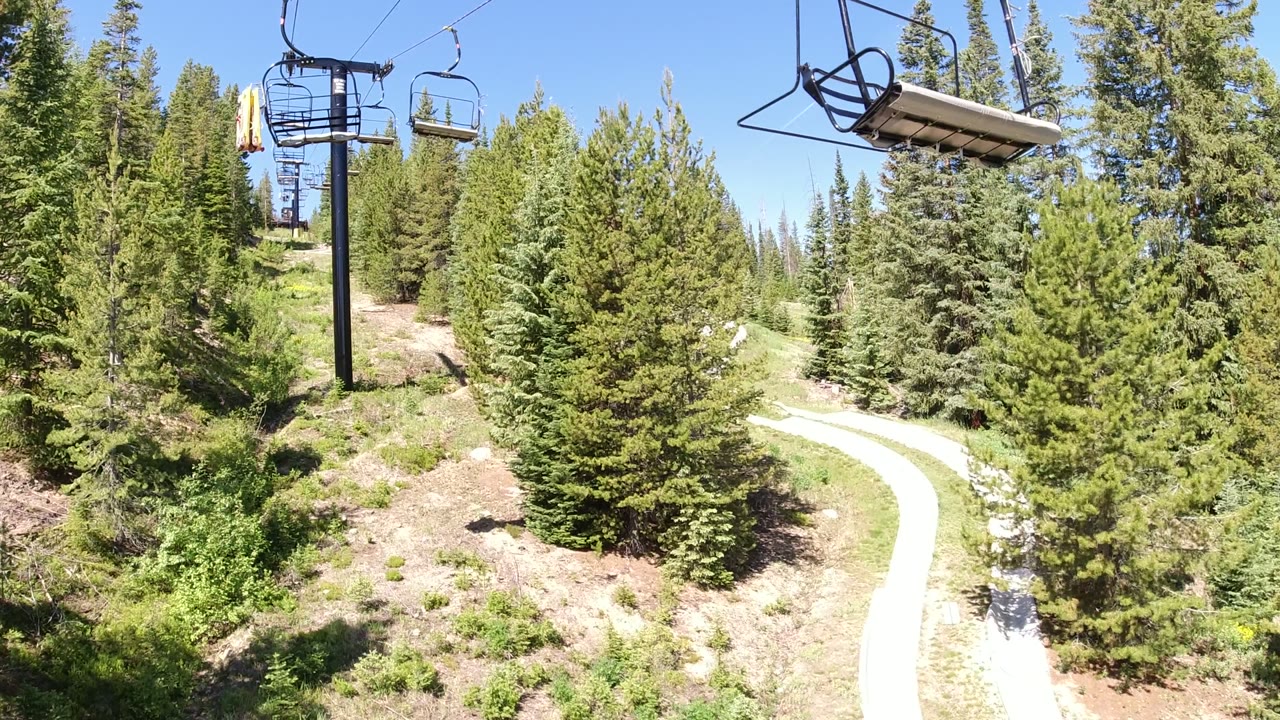 An empty lift chair and cable cross the upper frame above dense conifer trees in Winter Park, Colorado, with no visible people.