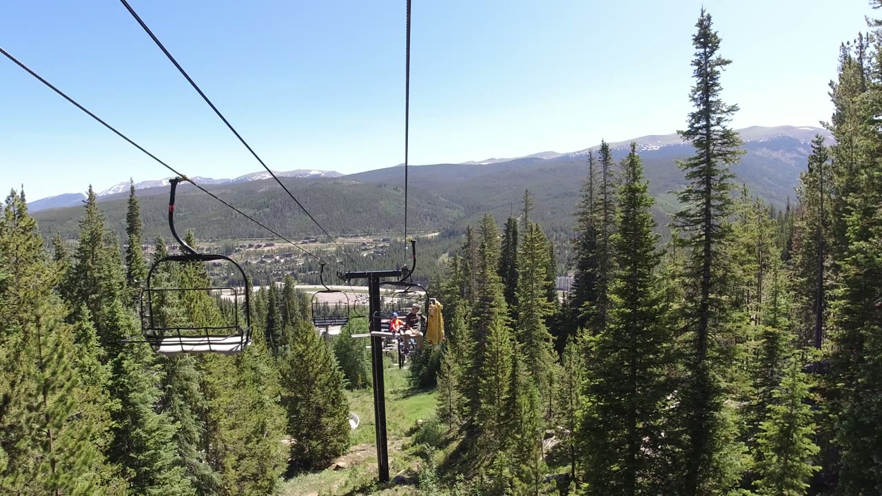 Chairlift cables over evergreen forest with distant mountains.