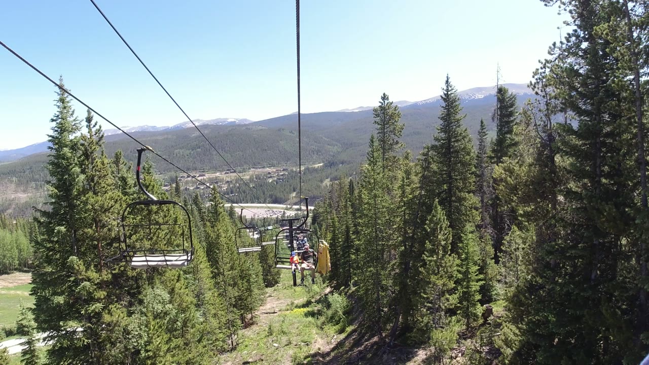 The Winter Park, Colorado lift line extends between tall conifers, with several chairs receding along the cable, a bright sky, and no clearly visible people.