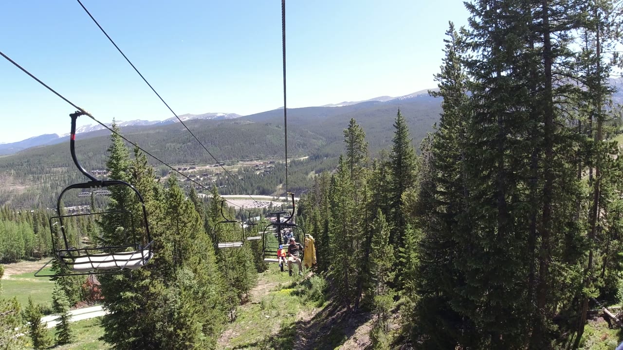 Ski lift chair and cables above evergreen trees with mountains in the distance.