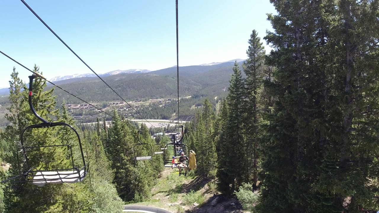 Chairlift cables over evergreen forest and distant mountains.