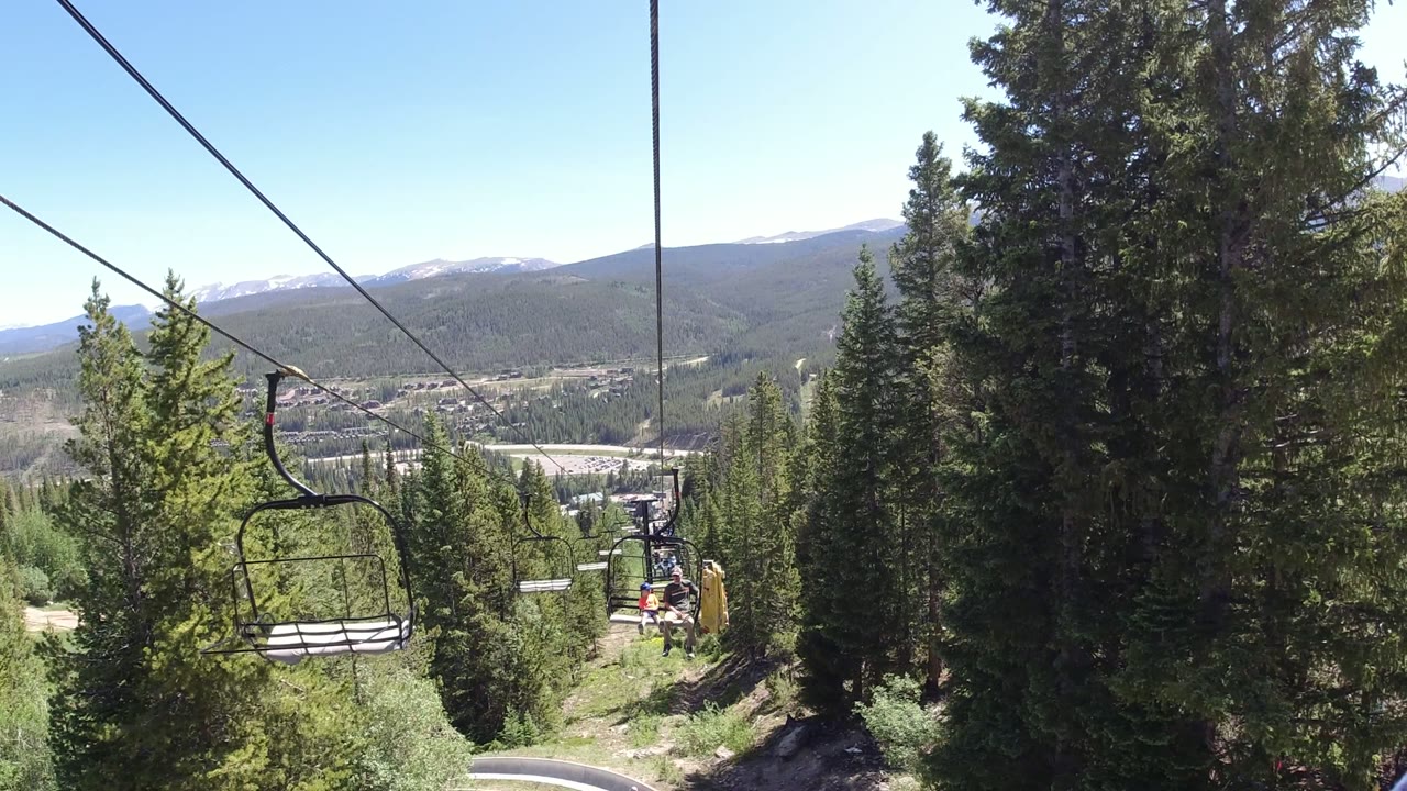A chairlift line in Winter Park, Colorado runs through tall evergreens toward a bright valley and distant mountains, with no visible people in the frame.