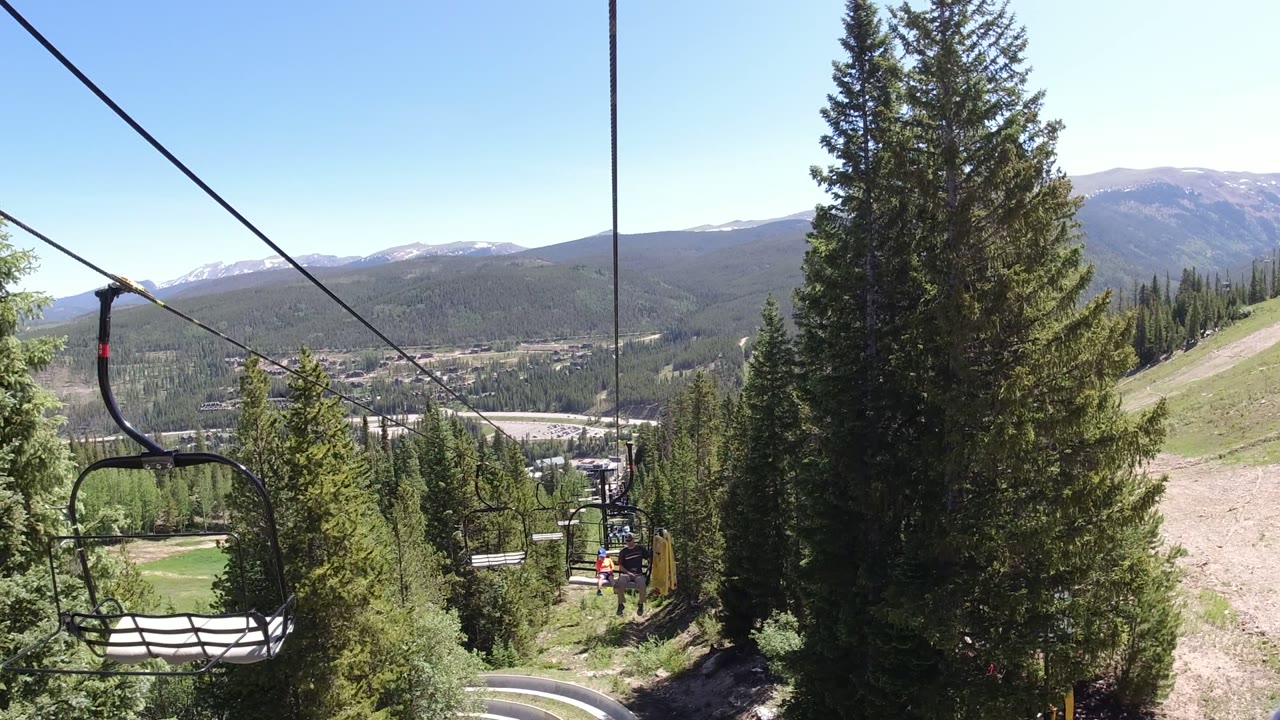 Open chairlift chair over evergreen trees and a mountain valley