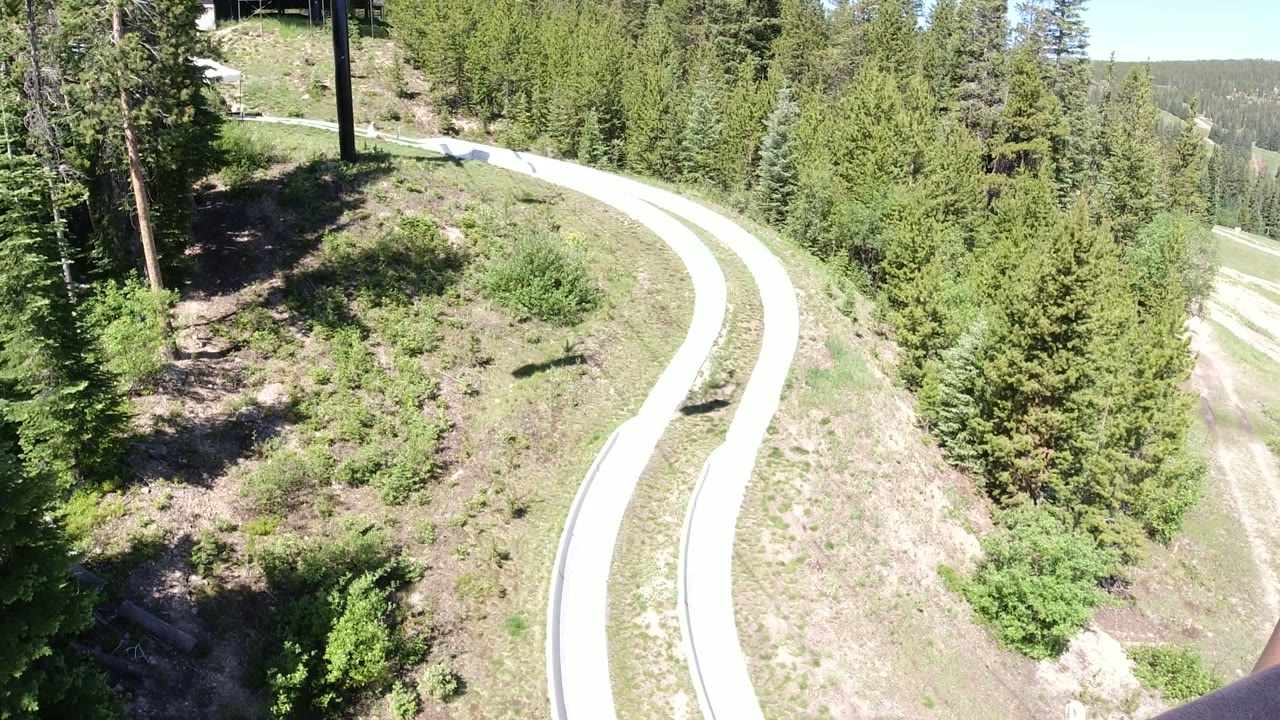 Winter Park, Colorado lift view with the bright path centered below, dark tree shadows at left, dense evergreens at right, and no visible people.