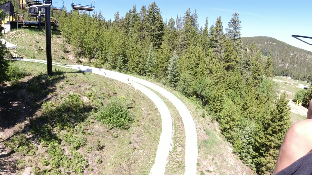 Chairlift view over a winding path and evergreen forest.