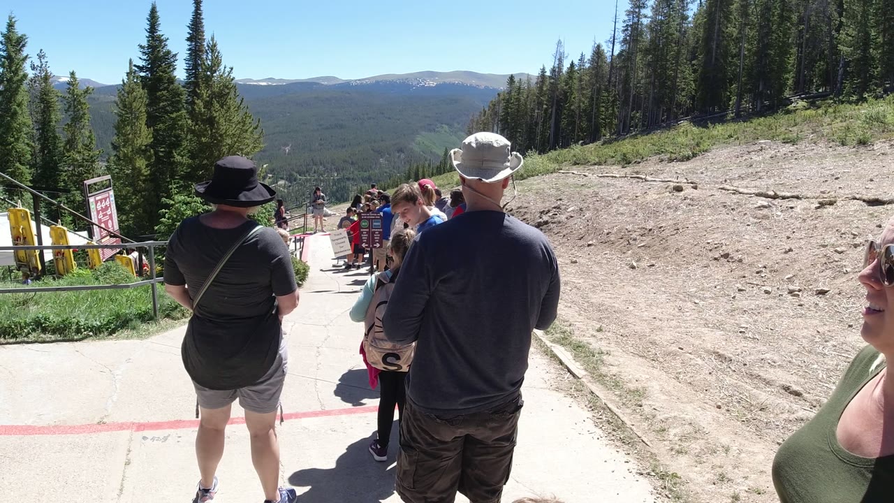Visitors standing in a mountain queue beside trees and railings.