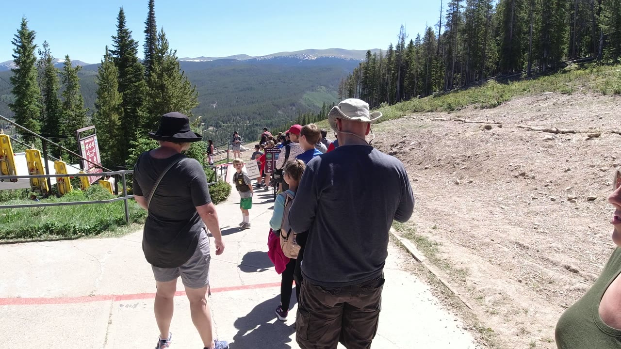 People waiting on a mountain walkway with trees and distant hills.