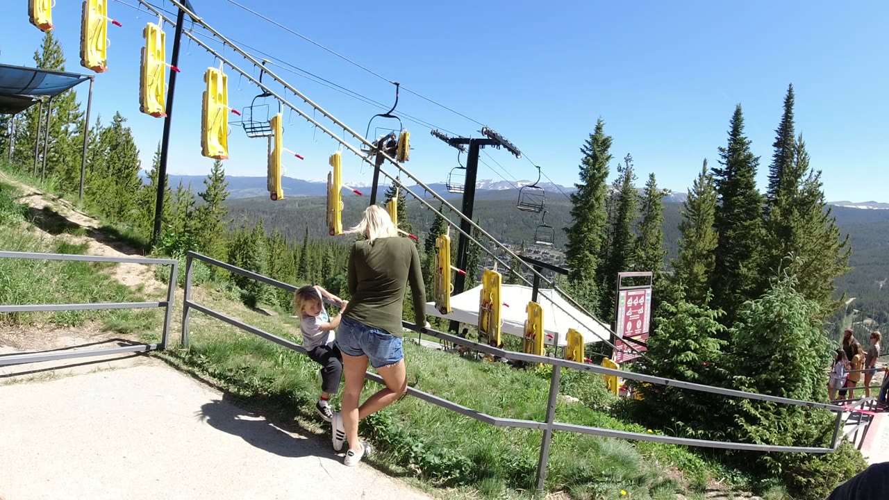Woman and child beside a rail on a mountain trail with lift cables overhead.