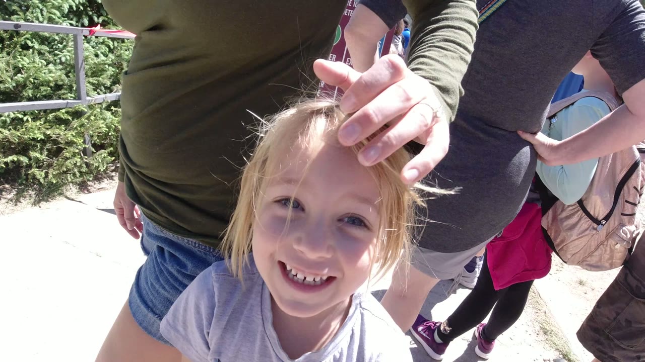 Smiling blonde child below cropped adults at an outdoor lift queue.