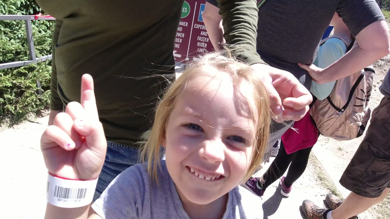 The child smiles and raises one finger near adults, wristband visible, with a lift sign and railing behind in Winter Park, Colorado.