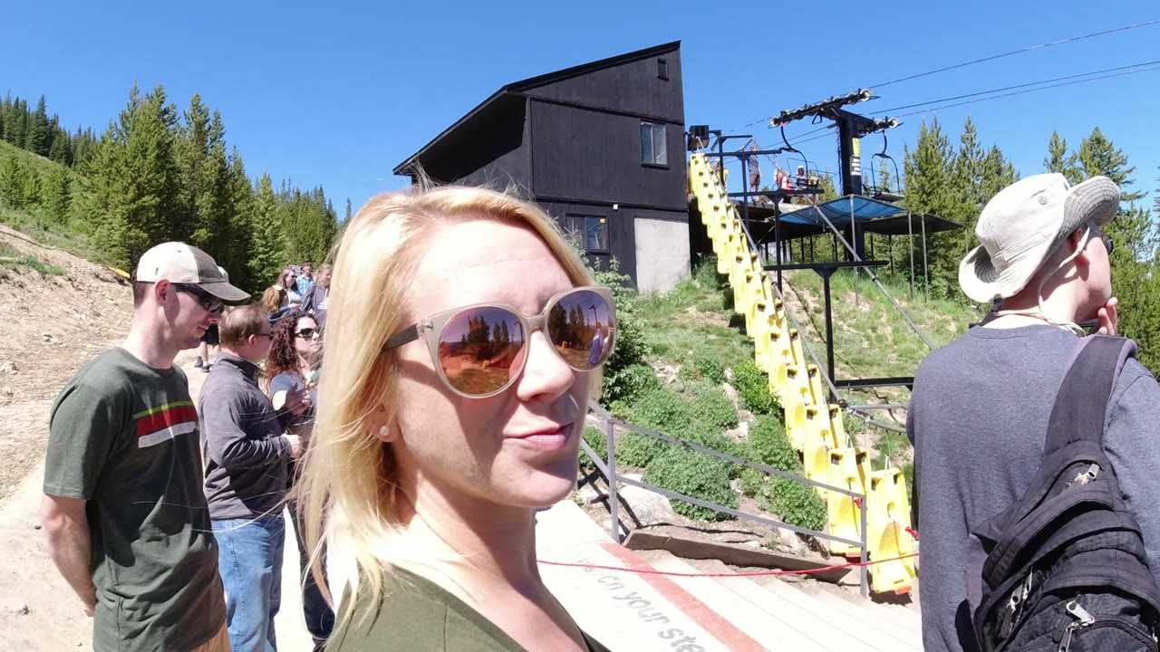 Blonde woman in sunglasses near tourists and a yellow lift structure.