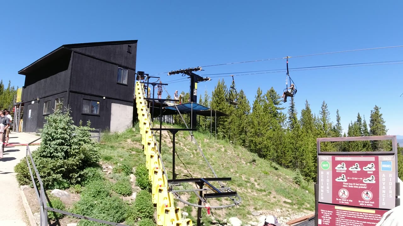Hilltop ropeway station with open chairlift seats and a red information sign.