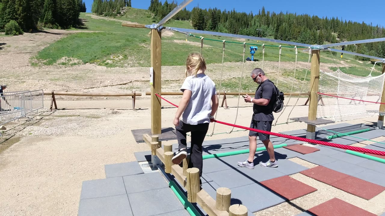 Girl and adult near a rope obstacle course on a sunny mountain playground.