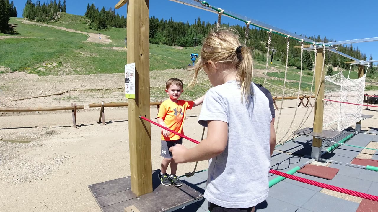 Girl holding a red rope near a boy on a ropes course platform.