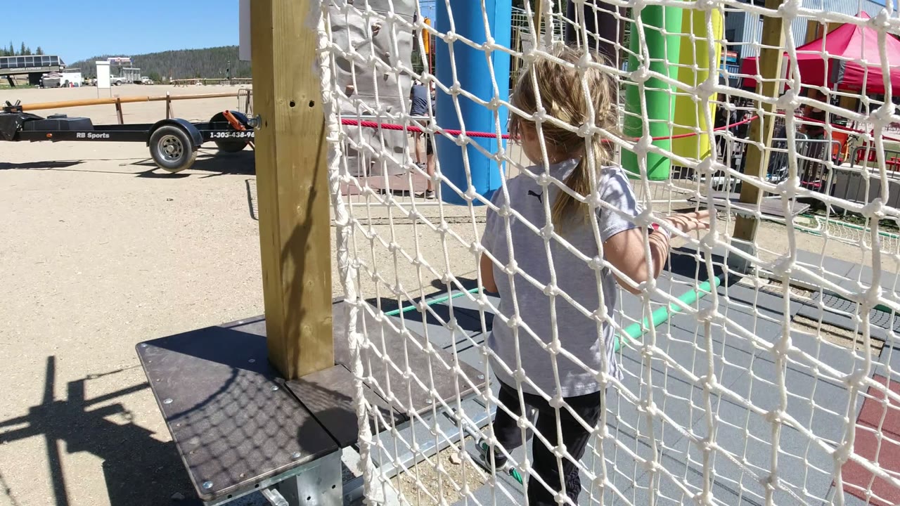 Young girl behind white rope netting on an outdoor playground.